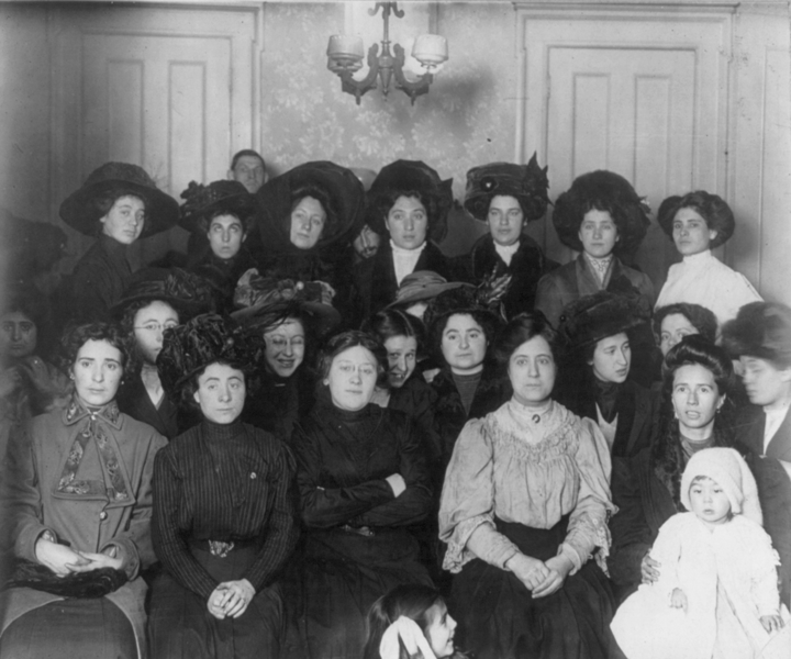 Black and white photo of a group of mostly women in old fashioned 1900's dresses and large hats.
